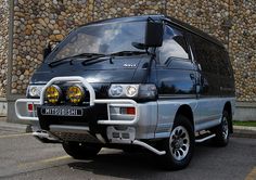 a silver van parked in front of a stone wall