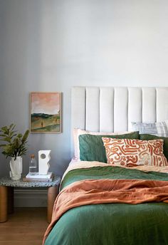 a bed with green and orange comforter next to a small side table in front of it