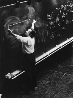 an old black and white photo of a man writing on a chalkboard with lights above it