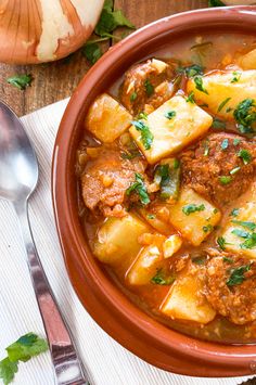 a bowl of stew with potatoes and meat in it next to a knife and fork