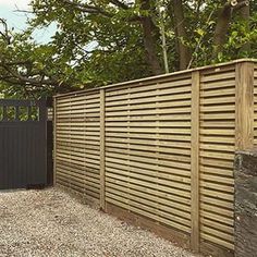 a wooden fence is next to a stone wall and some trees on the other side