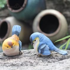 two small blue and yellow birds sitting on top of a rock next to vases