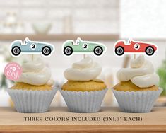 three cupcakes with white frosting and race cars on top, sitting on a table