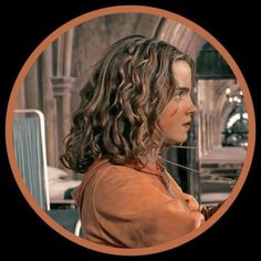 a woman with long curly hair sitting in front of a table and looking at something