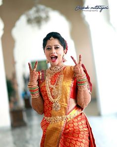 a woman dressed in an orange and gold outfit making the peace sign with her hands