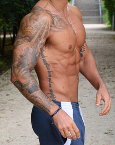 a shirtless man walking down a path with tattoos on his chest and arm,