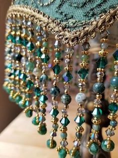 a green lamp with beads and chains hanging from it's side on a wooden table