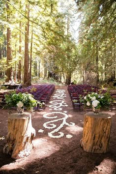 an outdoor wedding ceremony in the woods with wooden benches and chairs lined up on each side