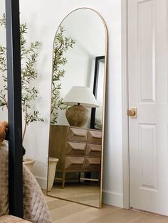 a large mirror sitting on top of a wooden floor next to a lamp and dresser