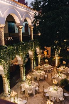 an outdoor dining area with tables and chairs covered in greenery, lit by candles