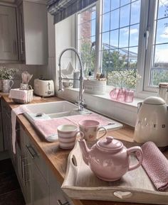 a pink tea set sitting on top of a kitchen counter next to a sink and window