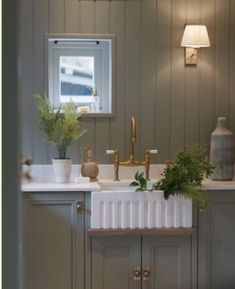 a white sink sitting under a window next to a green plant in a vase on top of a counter