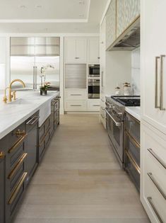 a large kitchen with white cabinets and gold handles on the countertops, along with stainless steel appliances