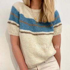 a blonde woman wearing a blue and white striped sweater posing in front of a white wall