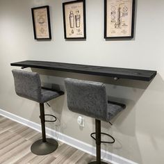 two gray bar stools sitting in front of a wall with pictures on the wall