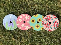 three painted discs sitting in the grass with flowers and leaves on them, one is pink, one is blue