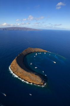 an island in the middle of the ocean with boats floating on it's surface