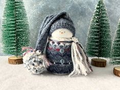 a snowman with a knitted hat and scarf next to small trees in the snow