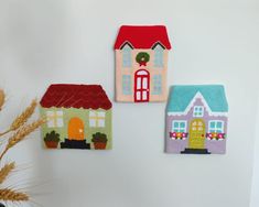 three felt houses are hanging on the wall next to a potted plant and vase