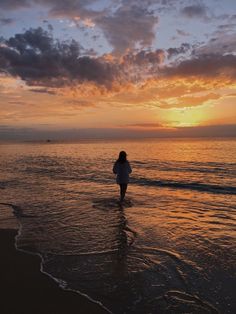 a woman walking into the ocean at sunset