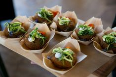 a person holding a tray with some food on top of it in paper cups and garnished with veggies