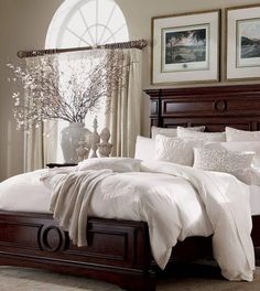 a bed with white comforters and pillows in a living room next to a window