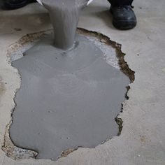 a man is pouring cement into a hole in the ground with his feet on it