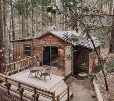 a small wooden cabin in the woods with lights strung from it's roof and deck