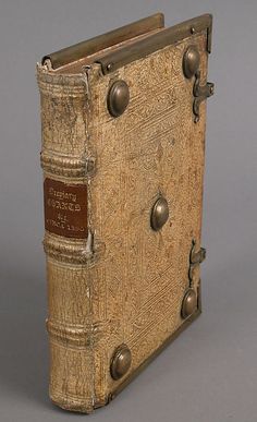 an old book with metal fittings on the front and back cover is sitting on a gray surface