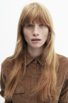 a woman with freckled hair is looking at the camera while wearing a brown shirt