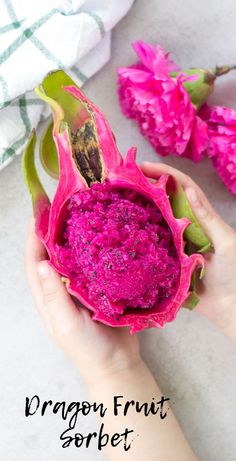 a person holding a dragon fruit sorbet in their hand with pink flowers behind it