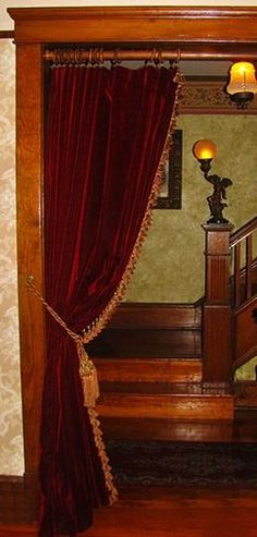 an image of a room with red curtains on the window sill and stairs to the second floor