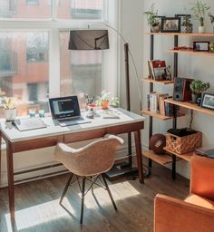 a laptop computer sitting on top of a wooden desk in front of a large window