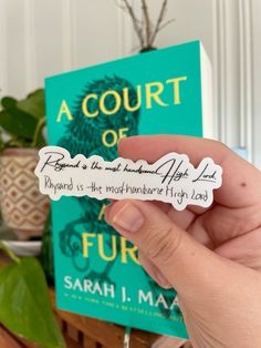 a person holding up a book in front of a plant and a sign that says, a court of four