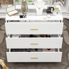 a white dresser with gold handles, drawers and jewelry on display in front of a mirror