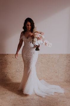 a woman in a wedding dress holding flowers and posing for the camera with her arms behind her back