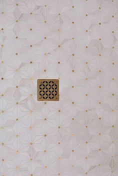 a white wall with gold dots and a square hole in the middle that is surrounded by smaller circles