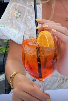 a woman holding up a glass with an orange slice in it and a straw sticking out of it