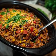 a black crock pot filled with chili, corn and cheese topped with cilantro