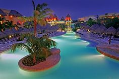 an outdoor swimming pool with chaise lounges and palm trees at night in the background