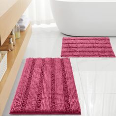 two bathroom rugs on the floor in front of a bathtub