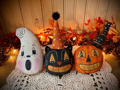 three painted pumpkins sitting on top of a doily next to some leaves and lights