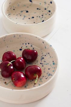 four cherries sit in a white bowl with blue speckles