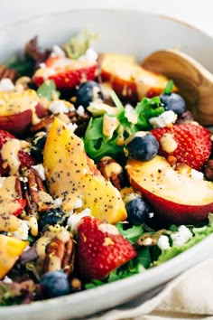 a salad with apples, blueberries, nuts and dressing in a white bowl on a table