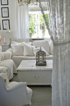 a living room filled with white furniture and a chandelier hanging from the ceiling