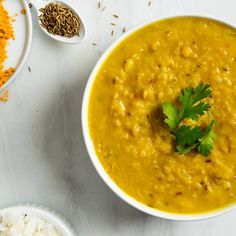 two bowls filled with soup next to some spices and spoons on a white table