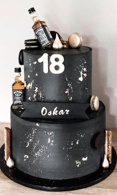 a three tiered black cake with bottles and spices on the top, sitting on a wooden table