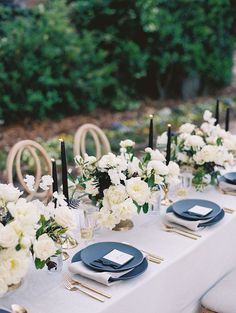 the table is set with white flowers and black plates