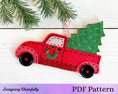 a red truck ornament with a christmas tree on it hanging from a pine branch