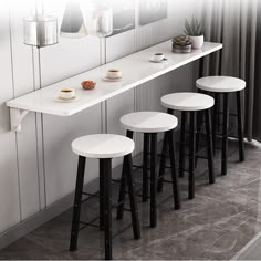 three white stools sitting next to each other in front of a counter with plates and cups on it